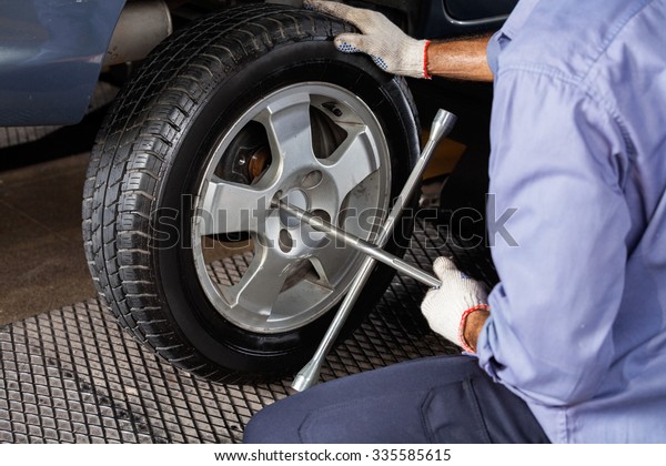 Midsection of mechanic fixing car tire with rim\
wrench at repair\
shop