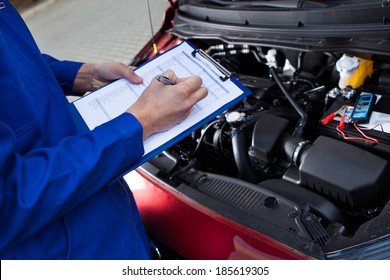 Midsection of mechanic holding clipboard in front of open car engine at street