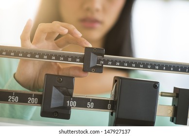 Midsection Of Mid Adult Asian Woman Adjusting Balance Weight Scale