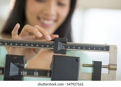 Midsection of mid adult Asian woman smiling while adjusting balance weight scale