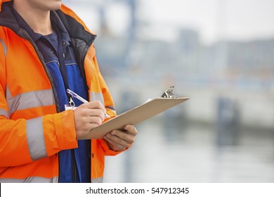 Midsection of mid adult man writing on clipboard in shipping yard
