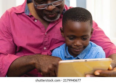 Midsection Of Multiracial Grandfather And Grandson Using Digital Tablet While Sitting At Home. Wireless Technology, Family, Childhood, Unaltered, Lifestyle And Retirement Concept.