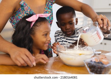 Midsection of multiracial mother pouring milk in bowl while standing with children in kitchen. Unaltered, family, togetherness, childhood, food, preparation, learning, lifestyle and home. - Powered by Shutterstock