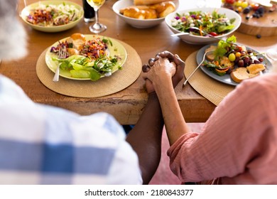 Midsection of multiracial senior couple holding hands while having lunch at dining table. Nursing home, meal, fresh, love, unaltered, togetherness, support, assisted living and retirement concept. - Powered by Shutterstock