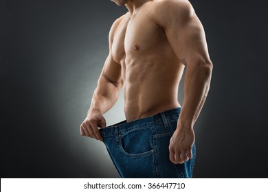 Midsection Of Muscular Man In Old Jeans Showing Weight Loss Against Black Background