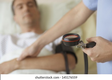 Midsection Of A Nurse Taking Blood Pressure And Pulse Of Patient In Hospital Bed