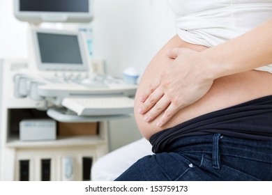 Midsection of pregnant woman touching her stomach in clinic before ultrasound