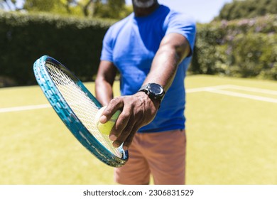 Midsection of senior african american man playing tennis preparing to serve on sunny grass court. Senior lifestyle, retirement, sport, summer, fitness, hobbies and leisure activities. - Powered by Shutterstock