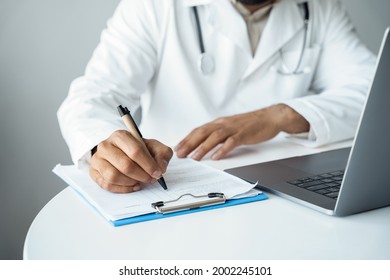 Mid-section Shot Of Arabian Male Doctor Hands Writing In Patient Checklist Form. Man Therapist At Desk Front On Laptop Computer. Medical Appointment, Online Healthcare Service, Remote Consultation