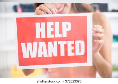 Midsection Of Smiling Female Owner Holding Help Wanted Sign In Retail Store