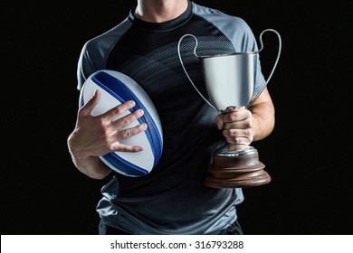 Midsection of successful rugby player holding trophy and ball against black background - Powered by Shutterstock