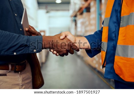 Midsection view of two male workers shaking hands at factory