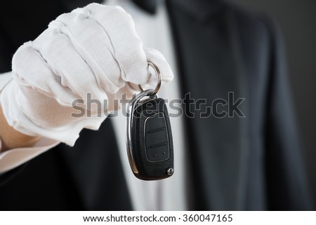 Midsection of waiter holding car key against gray background