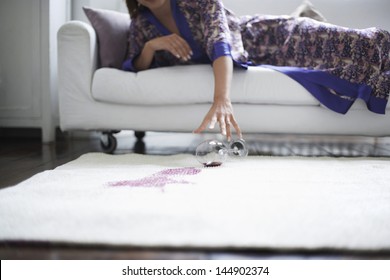 Midsection of woman reaching toward spilled wine glass on rug