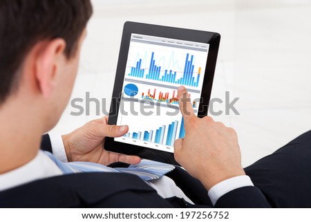 Midsection of young businessman comparing graphs on digital tablet in office