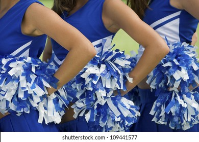 Midsection of young female cheerleaders holding pom-poms