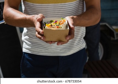 Midsection of young man holding tortilla in box while standing by food truck - Powered by Shutterstock