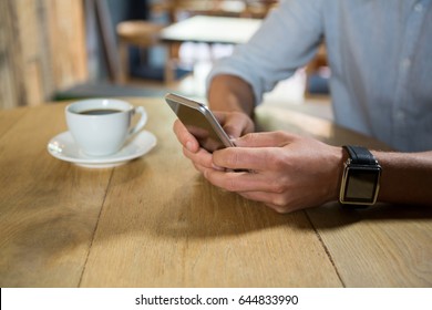 Midsection of young man using mobile phone at table in coffee shop