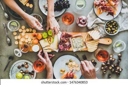 Mid-summer Picnic With Wine And Snacks. Flat-lay Of Charcuterie And Cheese Board, Rose Wine, Nuts, Olives And Peoples Hands Over Concrete Table Background, Top View. Family, Friends Holiday Gathering