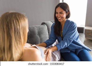Midwife examining expectant mother and satisfied with checkup. Young woman touching belly of pregnant patient lying on couch. Maternity and healthcare concept