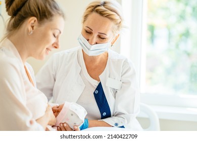 Midwife supporting a breastfeeding mother with her newborn baby girl in hospital ward. - Shutterstock ID 2140422709