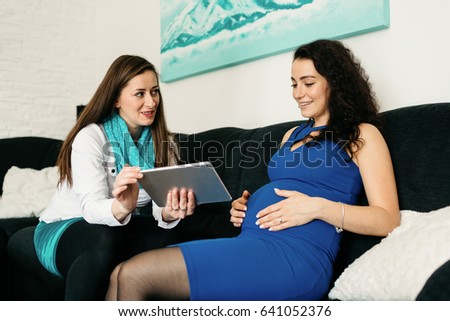 Midwife visiting an expectant mother and explaining on a tablet