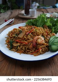 Mie Goreng or Stir fry noodles with vegetables and prawn in white plate. Wooden background.                       - Shutterstock ID 2256384693