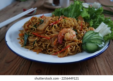 Mie Goreng or Stir fry noodles with vegetables and prawn in white plate. Wooden background.                       - Shutterstock ID 2256449121