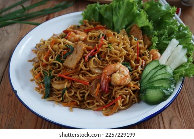 Mie Goreng or Stir fry noodles with vegetables and prawn in white plate. Wooden background                               - Shutterstock ID 2257229199