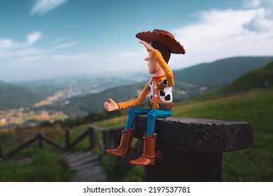 Miedzybrodzie Bialskie, Poland - August 3, 2022: Cowboy Woody From Toy Story Is Sitting On A Small, Wooden Bench Watching View On Valleys From The Mountain . Action Figure Model With His Hand To His E