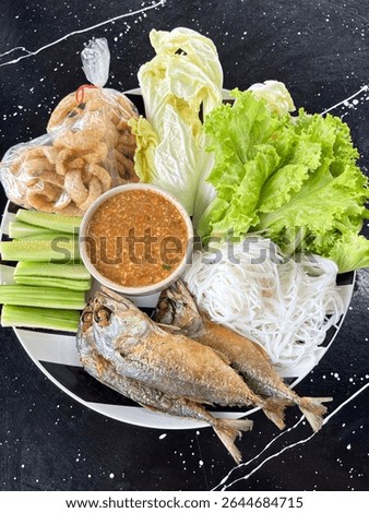 Mieng Pla Too is a Thai dish featuring fried mackerel, fresh vegetables such as lettuce, Chinese cabbage, and cucumber, served with rice noodles, savory dipping sauce, and crispy pork rinds