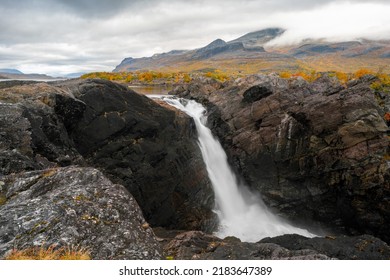 Mighty scenic waterfall under dramatic sky. Stuor Muorkke waterfall in Stora Sjofallet national park, Sweden. Adventure in arctic wilderness. Autumn colors in the arctic.