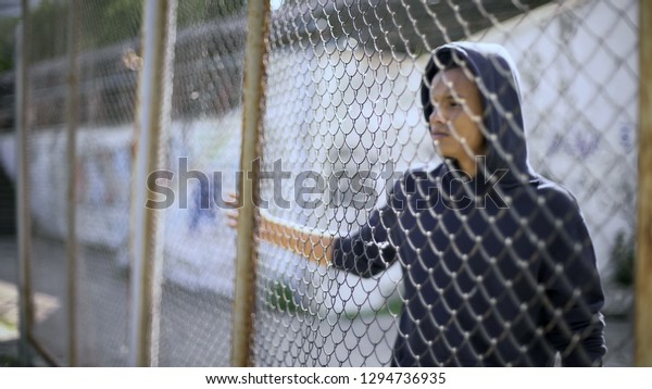 Migrant child separated from family,\
afro-american boy behind fence,\
detained