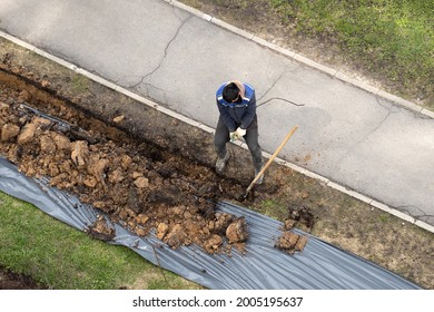 Migrant Labor. A Worker Digging A Ditch And Pulling An Armature.