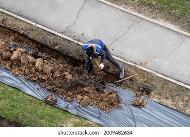 Migrant Labor. A Worker Digging A Ditch And Pulling A Piece Of Earth.