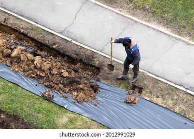 Migrant Labor. A Worker Digging A Ditch Along A Pavement In Summer.