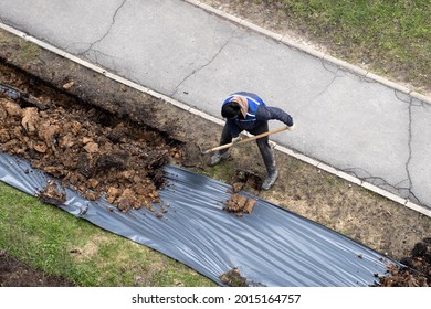 Migrant Labor. A Worker Digging A Ditch Along A Pavement In Summer.