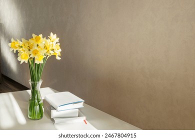 Miimal style. Bouquet of daffodils and stack of books on the white desk. Natural sun light