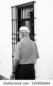 MIJAS, SPAIN - JULY 29, 2017: Old Spanish Man Walking Down The Street In Mijas In Black And White.