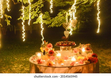 MILA, ITALY - Jul 07, 2021: A Cake On A Round Table With Flowers And Burning Candles Outdoors At A Wedding Venue At Night