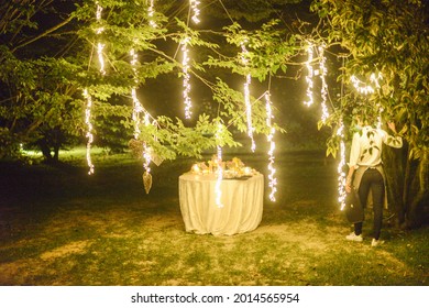 MILA, ITALY - Jul 07, 2021: A Small Round Table Outdoors At A Wedding Venue At Night With Bright Lights Hanging From Trees In Milan, Italy