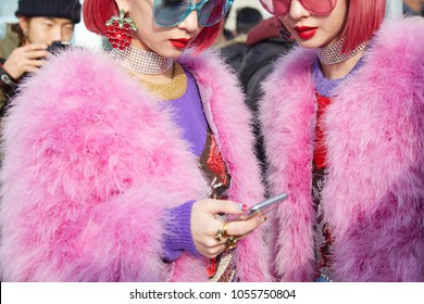 MILAN - FEBRUARY 21: Women With Pink Fur Coat And Hair Looking At Smartphone Before Gucci Fashion Show, Milan Fashion Week Street Style On February 21, 2018 In Milan.