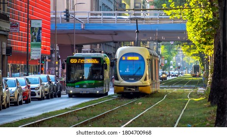 Milan Italy 08/25/2019: Public Transport Traffic On The Street Of The Autumn City In Lombardy. Old Yellow Tram. Modern Green Tram. Sun On An Autumn Day. Tram Rails. Green Bus. Covid Period 19