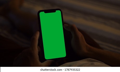 Milan, Italy - August 202: Holding A Green Screen IPhone, Lying On The Bed At Dusk