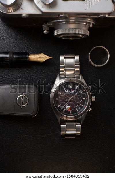 Milan, Italy - December 6, 2019: still life of a\
Sector No Limits 770 wristwatch for man, resting on black\
background. A Mont Blanc pen, a ring and a Leica film camera and\
car keys are visible too