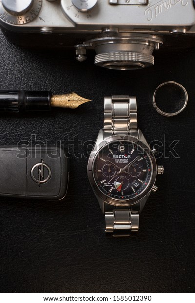 Milan, Italy - December 6, 2019: still life of a\
Sector No Limits 770 wristwatch for man, resting on black\
background. A Mont Blanc pen, a ring and a Leica film camera and\
car keys are visible too