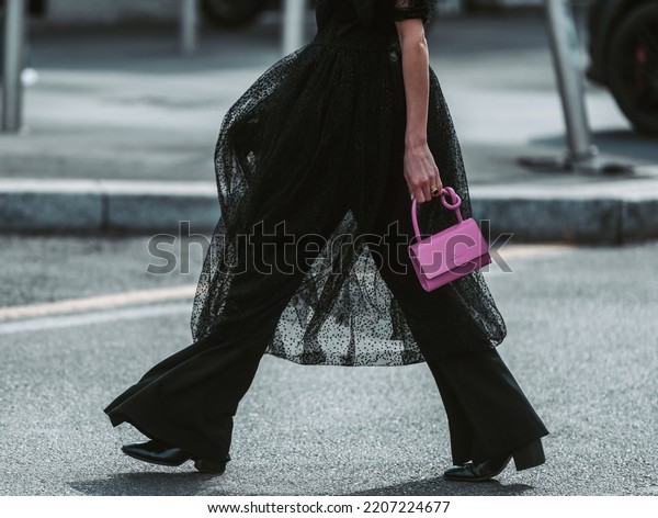 Milan, Italy - February 24, 2022: Street style,\
woman wearing puffy sleeves midi dress, high waist black flared\
pants, pink leather crocodile print pattern handbag and black shiny\
leather heels shoes