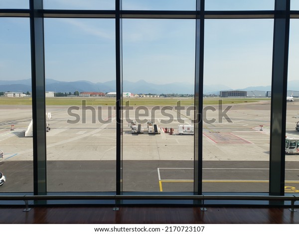 Milan, Italy - June 2022: View from the glass\
windows of the gate lounge in Milan Bergamo BGY airport on the\
apron with ground handling services\' vehicles parked  during a\
sunny day in Italy