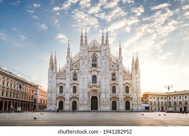 Milan, Italy - March 2021: View of the Milan Cathedral with empty square due to the coronavirus blockade, with blue sky with white clouds and glow of light from the newly risen sun