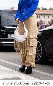 Milan, Italy - September, 21, 2022: Woman In Blue Denim Asymmetric Cropped Jacket, Leather Bag With Nailed Studded Fringed Chain Pendant Shoulder, Beige Cargo Flared Pants, Platform High Heels Shoes.